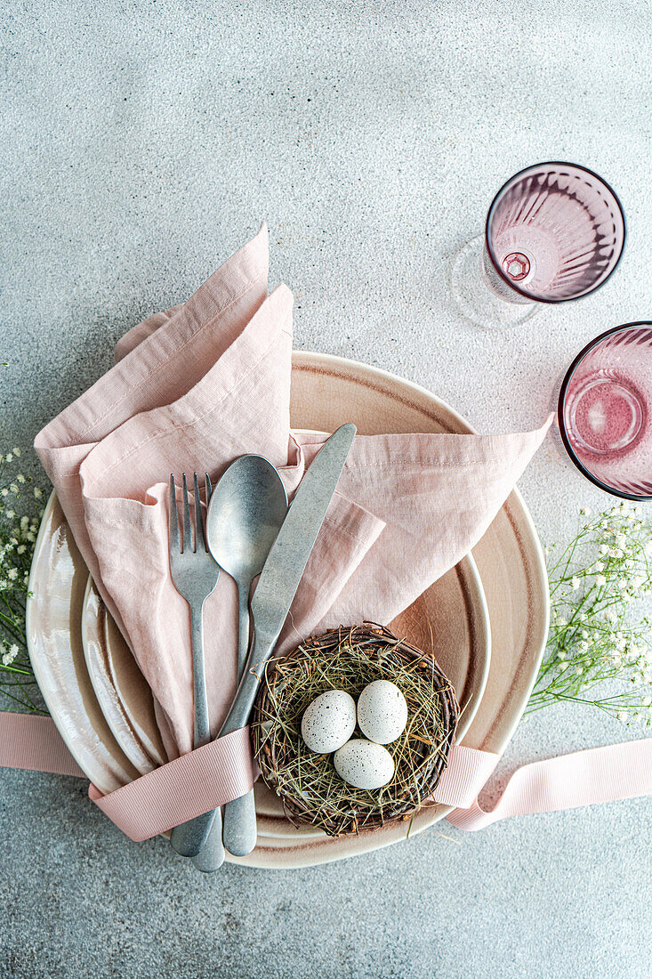 From above aesthetically pleasing Easter table arrangement featuring a nest with speckled eggs, nestled on stacked ceramic plates with a pink linen napkin.