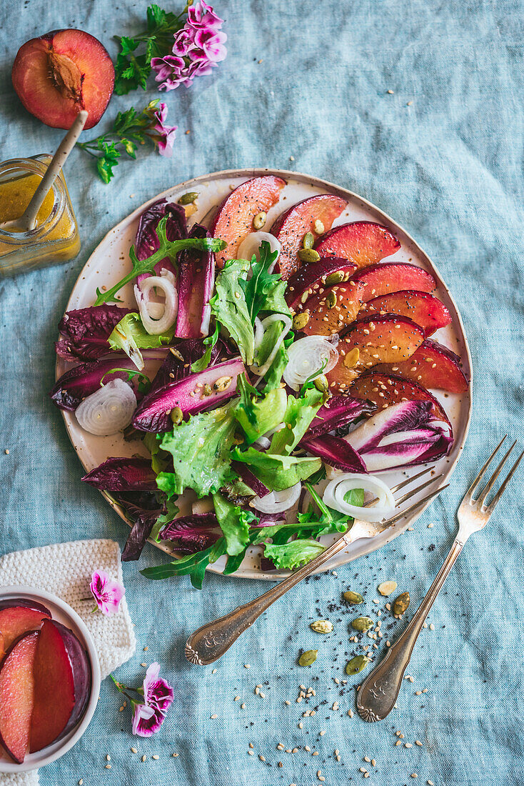 Draufsicht auf einen leckeren gesunden gegrillten Pflaumen-Endivien-Salat mit verschiedenen Gemüsesorten und Gewürzen auf dem Tisch