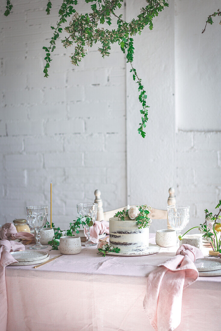 Elegant table served with plates and flowers placed near yummy cake on pink tablecloth against brick wall