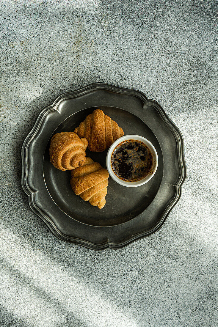 Draufsicht auf einen schwarzen Kaffee und frisch gebackene Croissants auf einem Betontisch