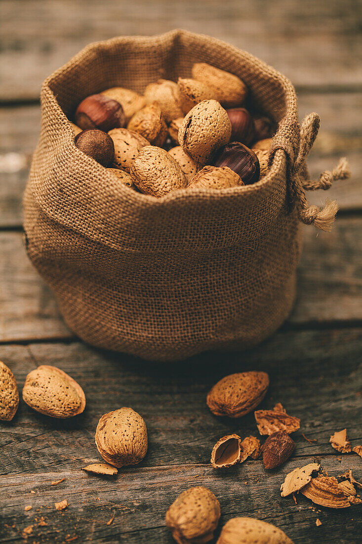 Almonds escape from a burlap bag, scattering on a weathered wooden table, capturing a sense of harvest abundance.