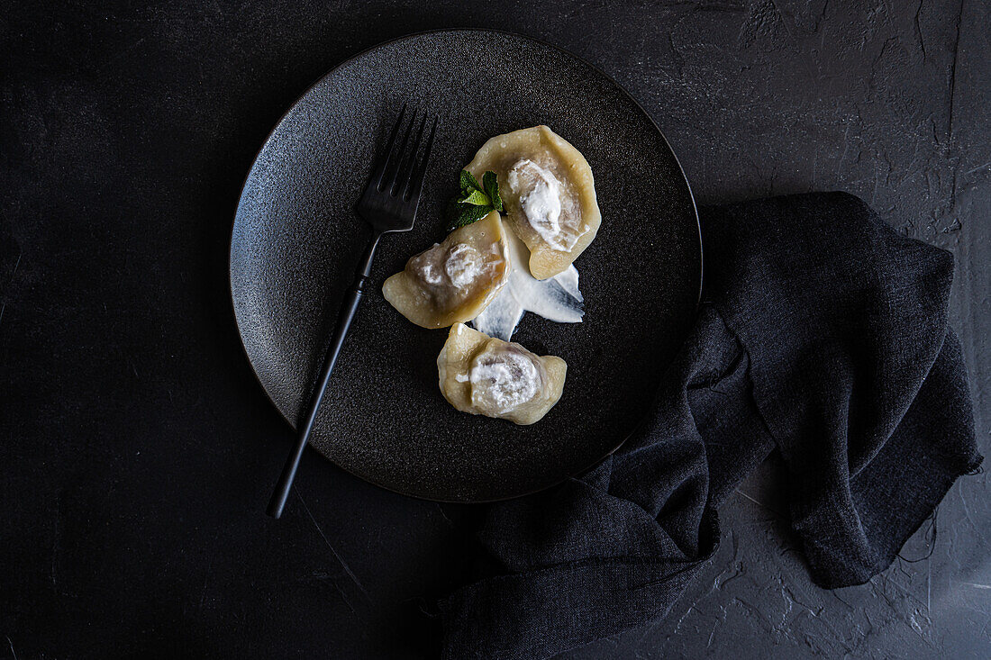 Top view of a tasty traditional Ukrainian dumplings with cherry and sour cream with mint