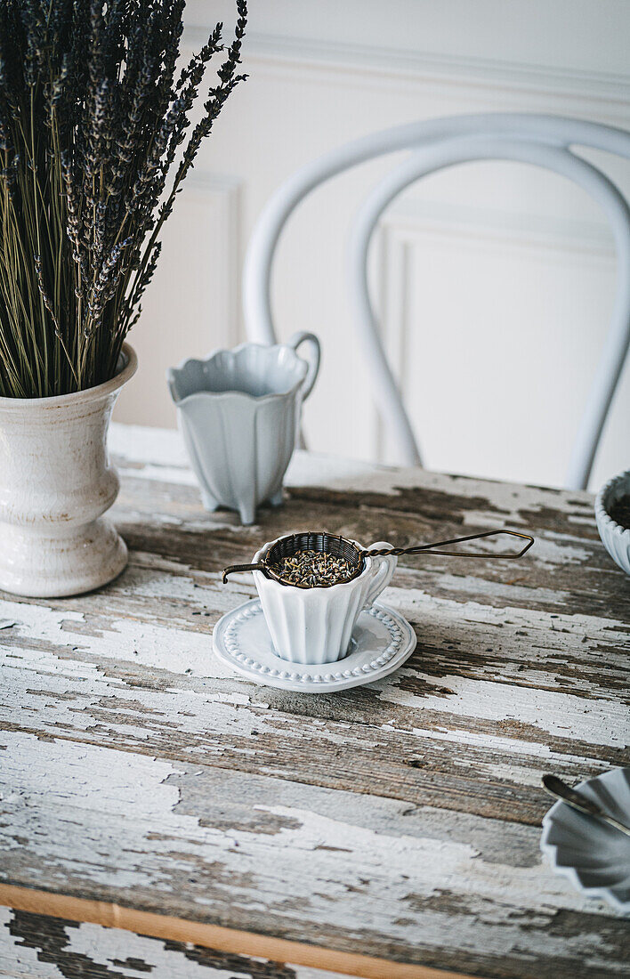 Weiße Keramiktasse mit aromatischem Tee und frischen Lavendelblüten auf einem Holztisch