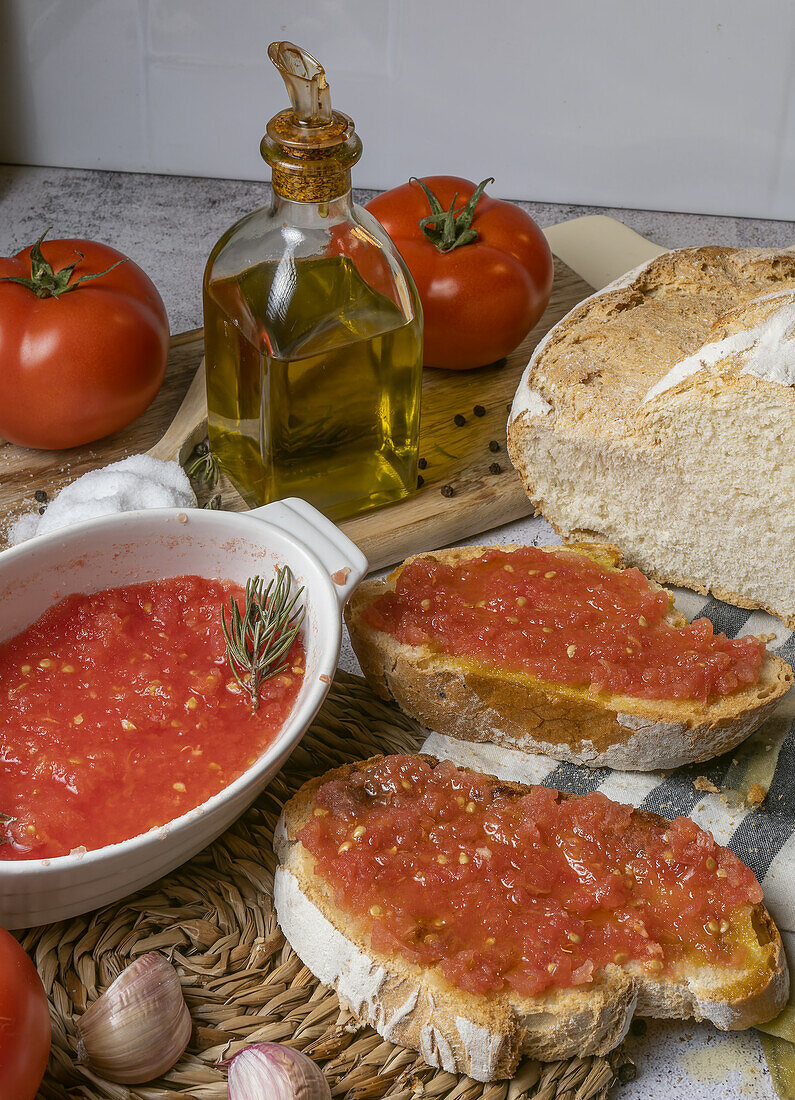 From above of pieces of bread with tomato spread placed on table near bowl with tomato spread, bottle of olive oil and fresh tomatoes