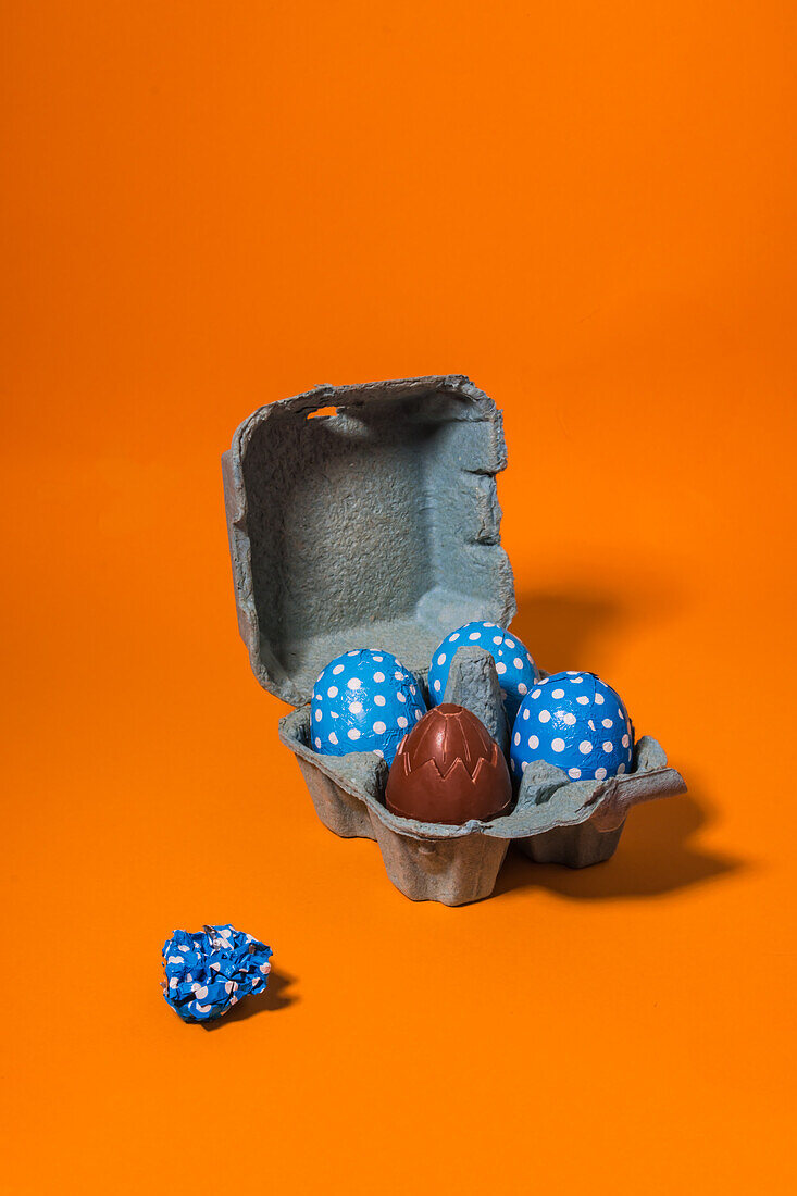 Close-up of some blue easter eggs inside a gray cardboard box on an orange background