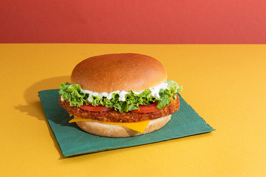 Leckerer Fisch-Burger mit Tomaten, Käsescheiben und frischem Salat auf gelbem und rotem Hintergrund