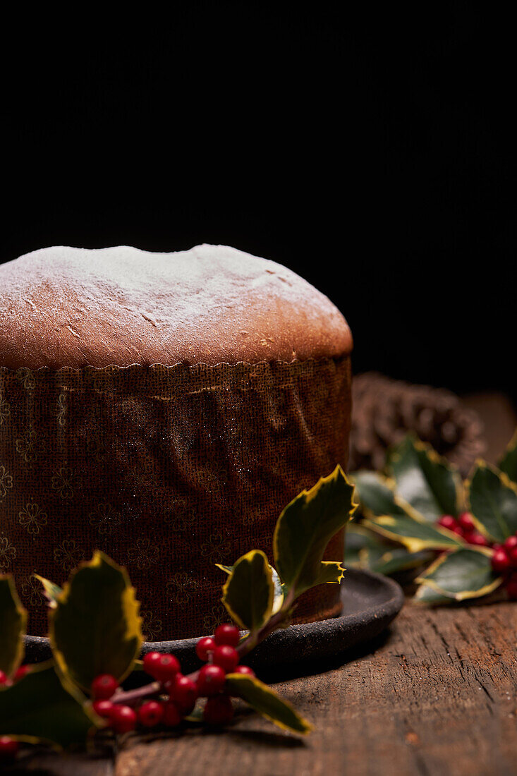 A panettone sprinkled with powdered sugar is complemented by bright red berries and lush green leaves, evoking a festive holiday feel