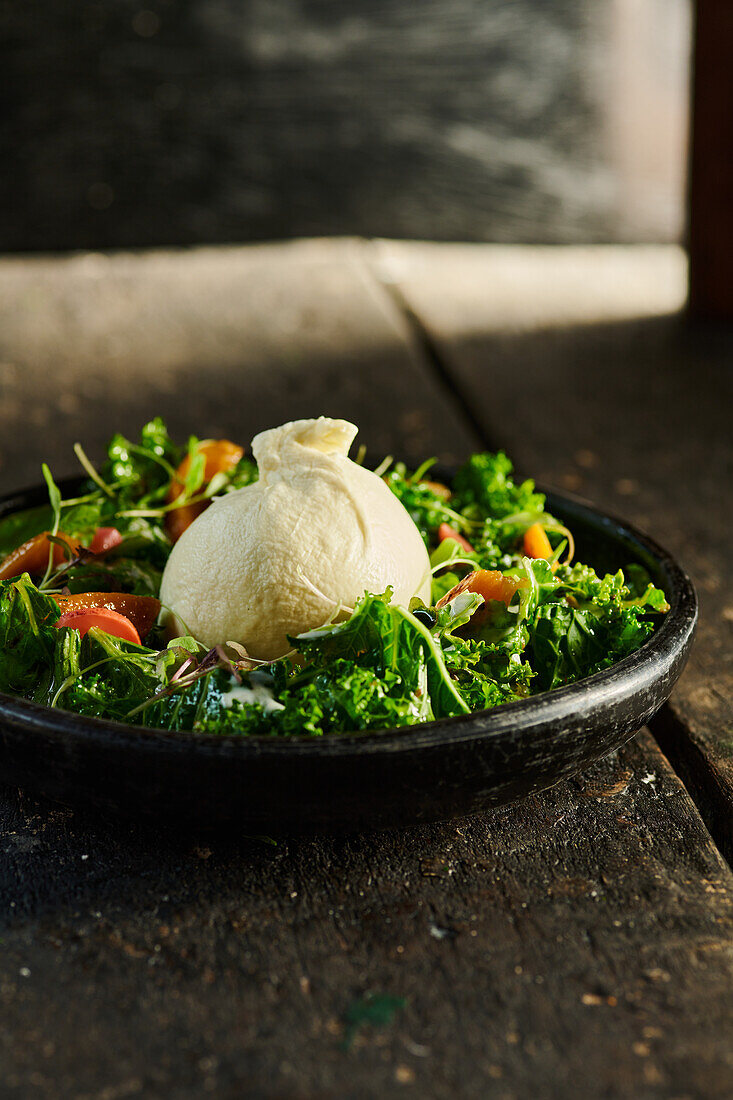 High angle of appetizing broccoli and carrots served on black plate with burrata cheese placed on wooden table