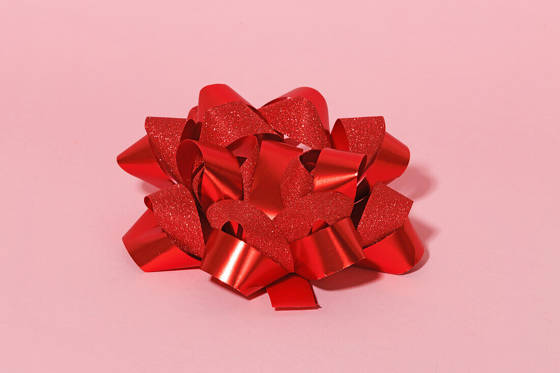 Generatives AI-Bild einer glitzernden roten Schleife auf glattem rosafarbenem Hintergrund, als Beispiel für ein Geschenkkonzept zum Valentinstag