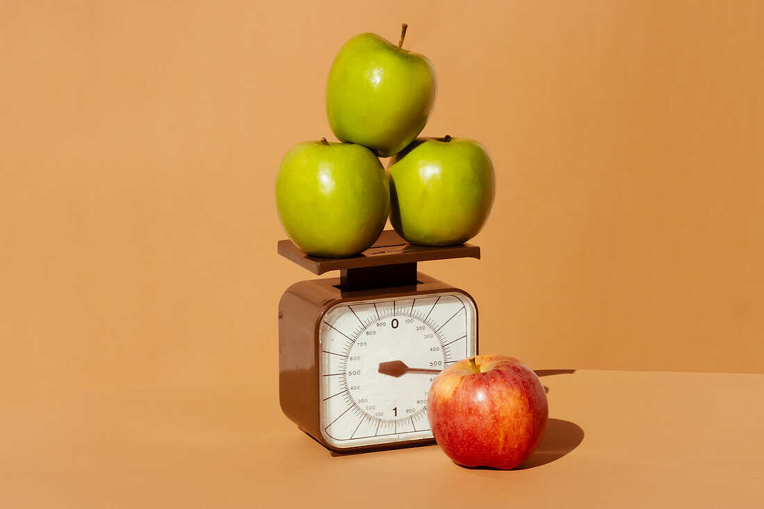 Frische und saftige rote und grüne Äpfel auf einer Waage als Teil einer gesunden kalorienkontrollierten Ernährung auf farbigem Hintergrund