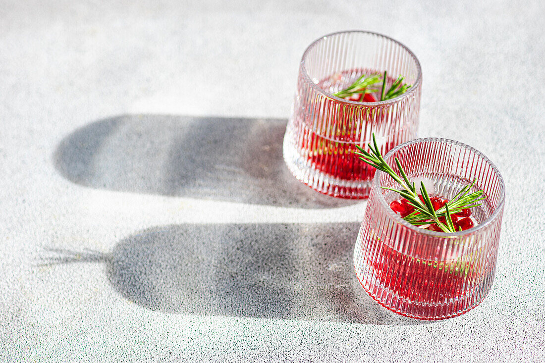 From above of sunlit gin tonic cocktails with pomegranate and rosemary in textured glasses on a bright surface