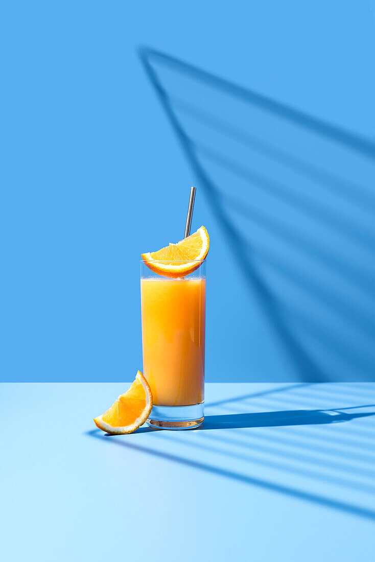 Gepresster Orangensaft garniert mit Orangenscheibe auf blauem Hintergrund