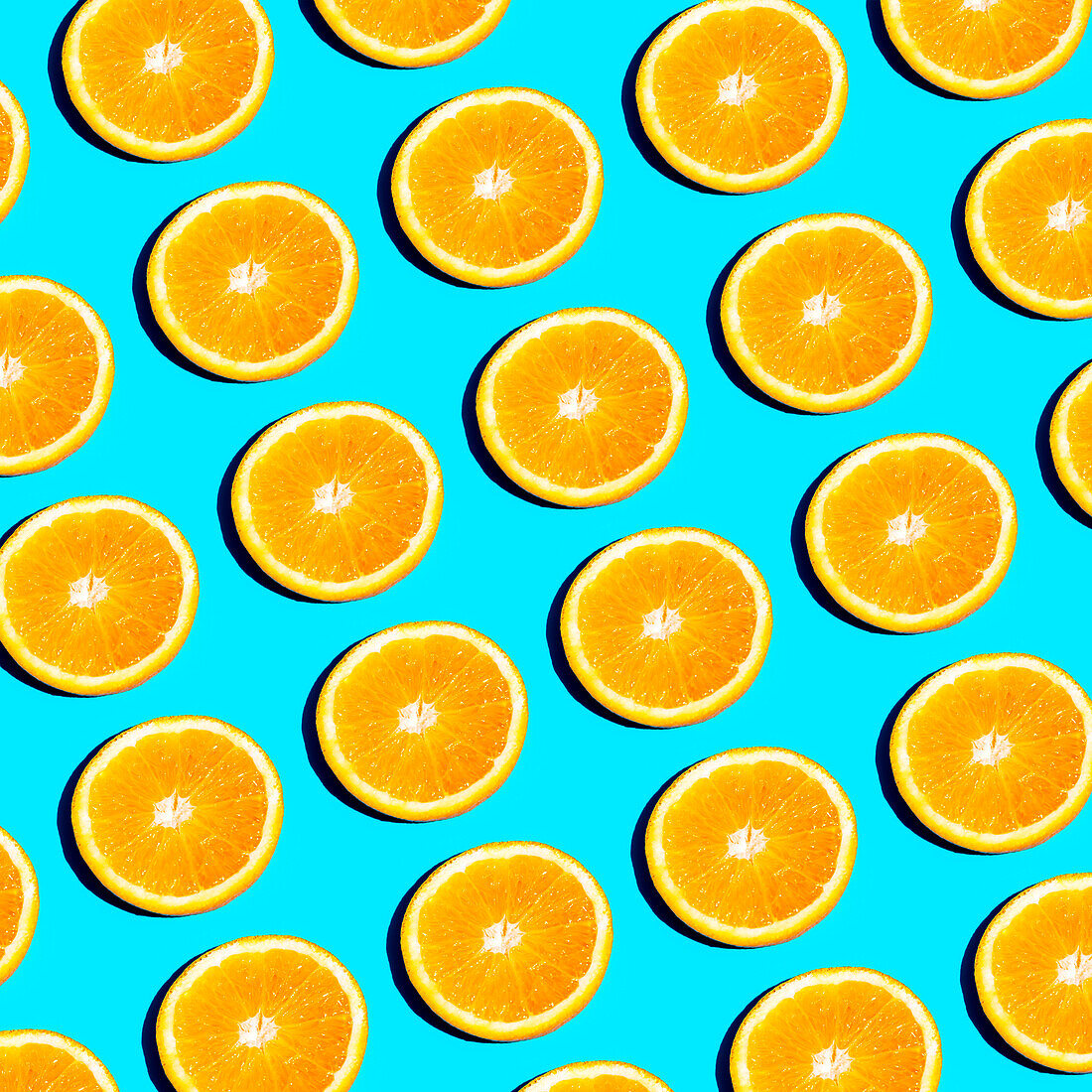 From above slices of vibrant orange citrus fruit arranged in a repetitive pattern on a bright blue background, creating a fresh and summery feel