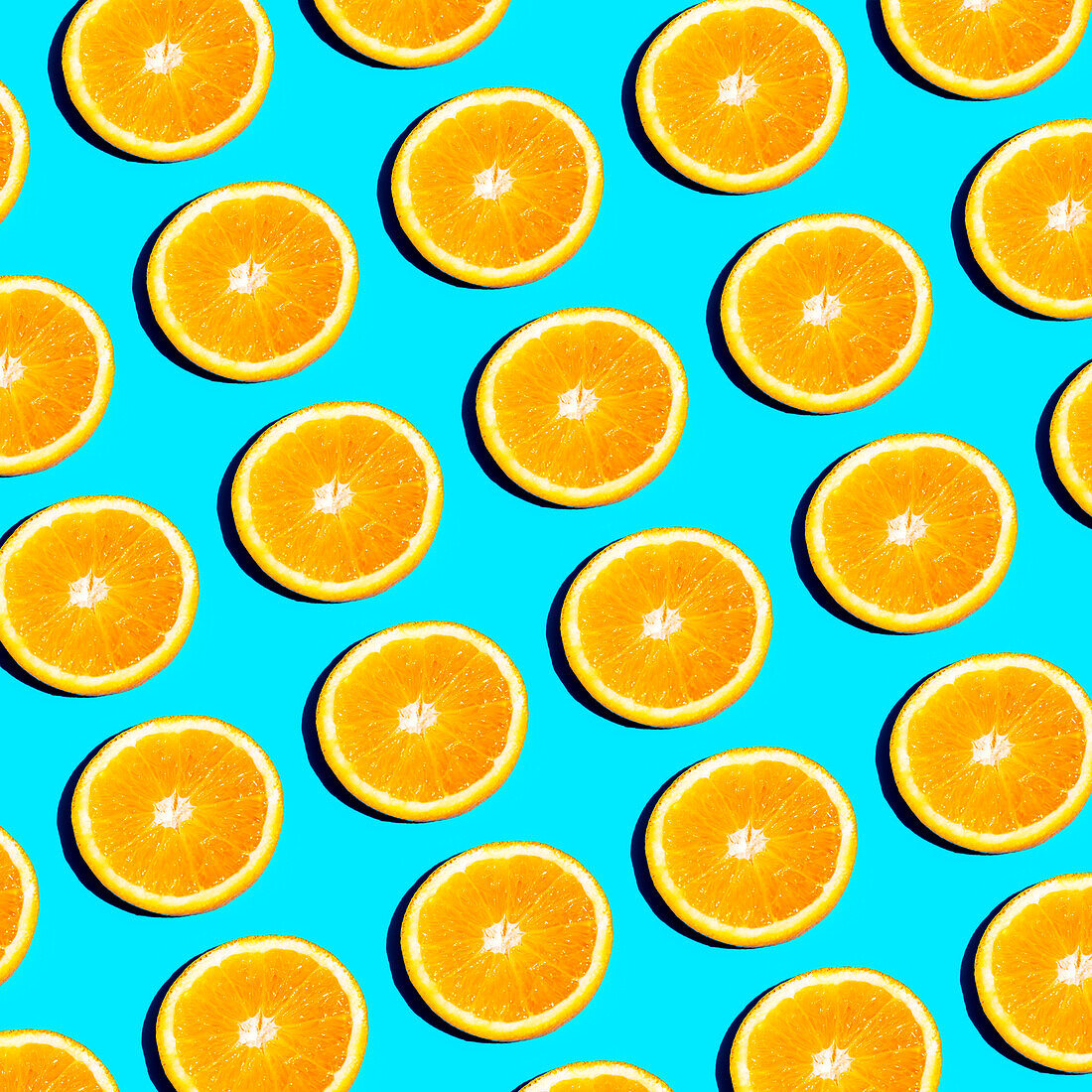 Von oben: Scheiben von leuchtend orangefarbenen Zitrusfrüchten, die in einem sich wiederholenden Muster auf einem hellblauen Hintergrund angeordnet sind und ein frisches und sommerliches Gefühl vermitteln