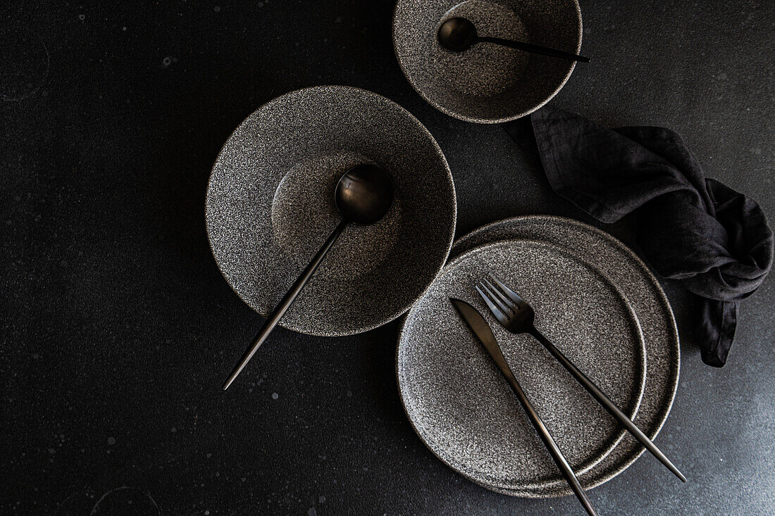An aesthetic arrangement of dark stoneware dishes with a rustic charm, set on a dark textured background, highlighting minimalistic tableware design.