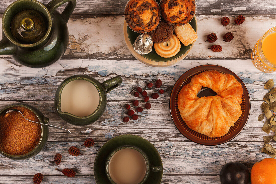 Draufsicht auf einen Holztisch mit Teetassen, einer Teekanne, Kuchen und verstreuten getrockneten Blättern, die eine gemütliche herbstliche Atmosphäre heraufbeschwören