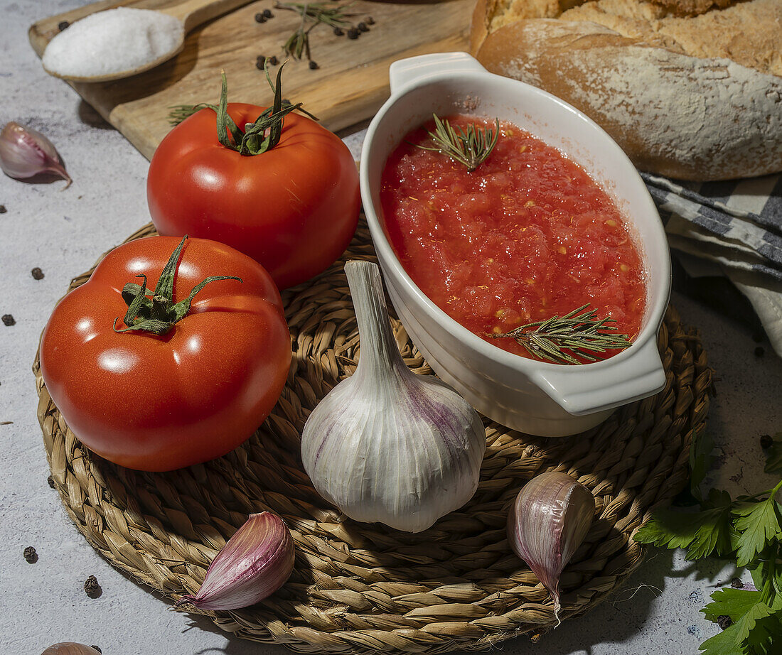 From above ripe tomatoes and unpeeled garlic placed on table near bowl with crushed tomatoes, wholegrain bread on napkin and chopping board