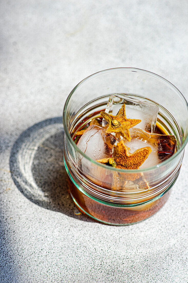 High angle of glass of whiskey with ice and orange peel placed on gray background