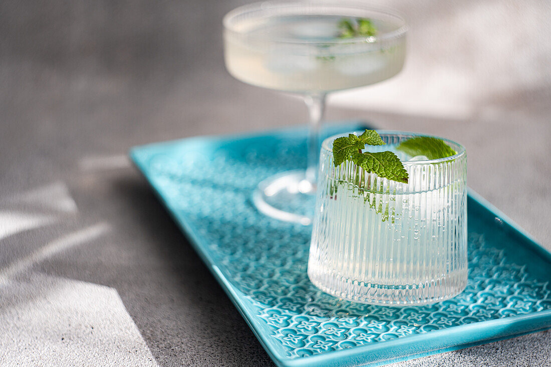 An elegant glass cocktail and a unique ice cube on a blue textured tray, both garnished with fresh mint leaves, under soft lighting