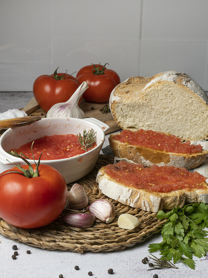 Pieces of bread with ripe tomatoes and greens placed on table against bowl with tomato spread and garlic