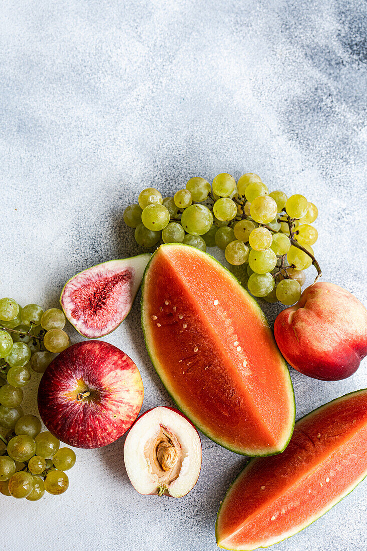 Draufsicht auf einen Rahmen mit Früchten der Saison, bestehend aus Wassermelone, Weintrauben und Äpfeln, auf einer weißen Fläche