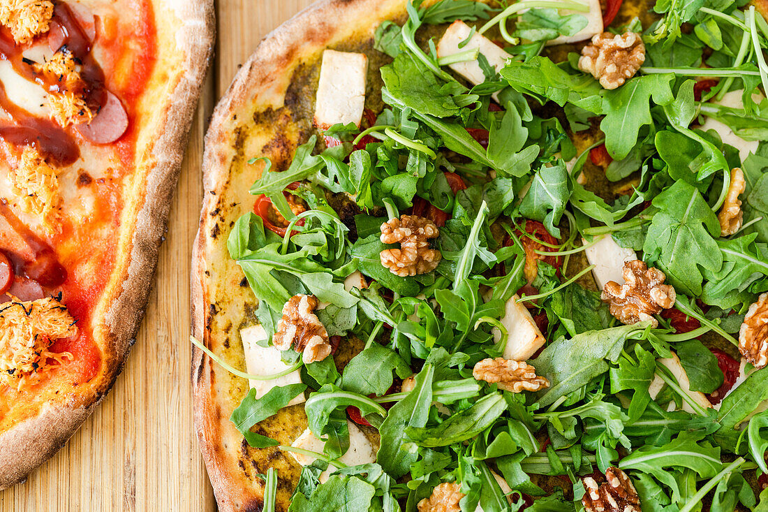Draufsicht auf eine leckere vegetarische Pizza mit Käse und Walnüssen und grünen Salatblättern auf einer Holzunterlage