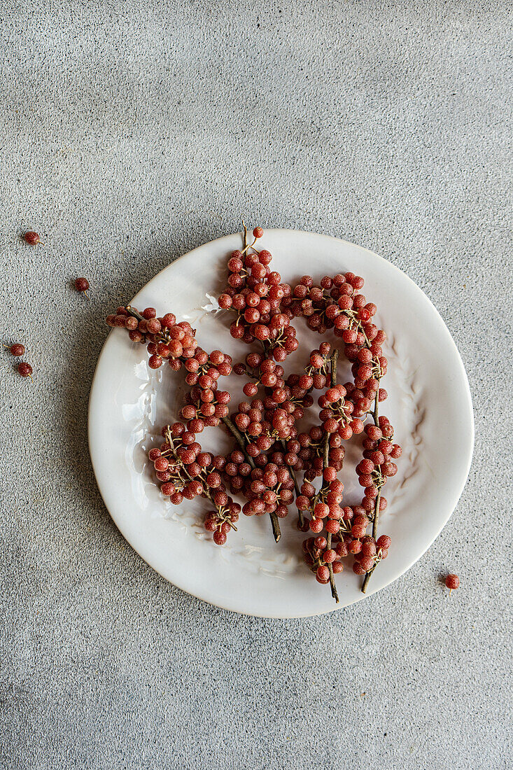 From above of scattered organic buffaloberries on a white ceramic plate with a few berries fallen on the grey surface in soft daylight