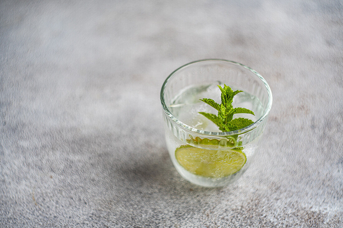 From above glass of summer lemonade with tonic and fresh lime and mint leaves placed on gray surface during summer season at home