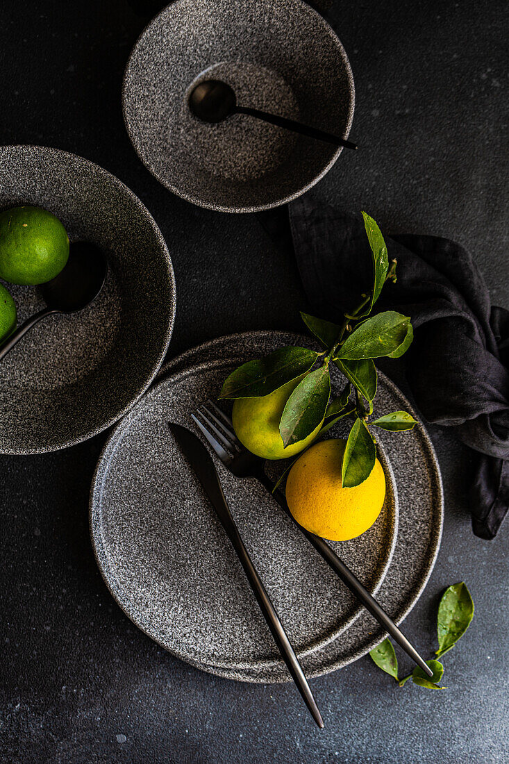 A sophisticated table setting featuring gray ceramics, fresh citrus, and a dark, moody background.