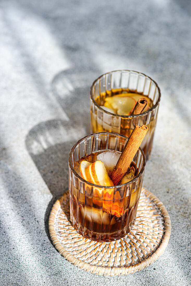 Von oben auf frischen Apfelwein-Cocktails garniert mit Zimtstangen, Sternanis und Apfelscheiben in einem mit Eiswürfeln gefüllten Kristallglas auf einem strukturierten Hintergrund