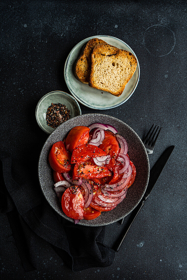 Bowl with salad with farm organic tomatoes and red onion with flax seeds and sea salt and toast on black background