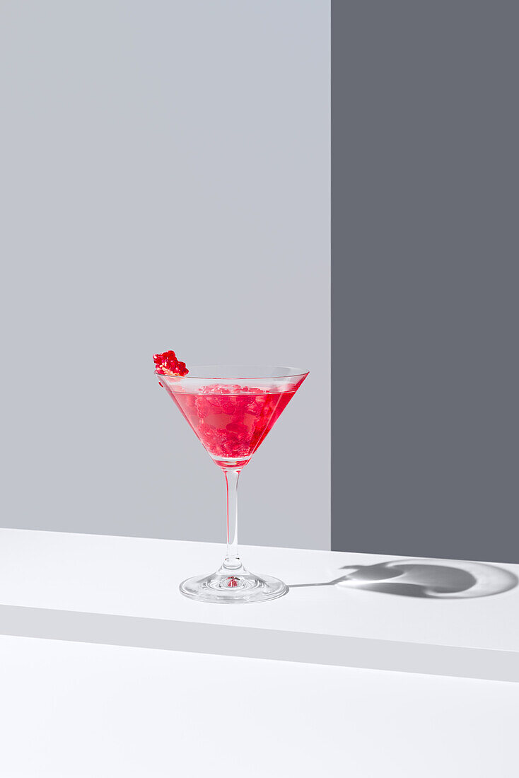 Glas mit rotem Granatapfelcocktail und Granatapfelkernen vor einem grauen Hintergrund, der einen weichen Schatten wirft