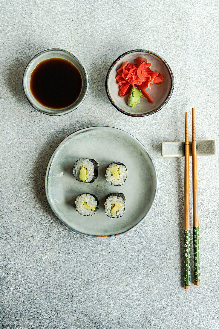 Blick von oben auf ein japanisches Essensset mit Avocado-Maki-Rolle und gebratenem Sushi mit Sojasauce und Ingwer auf einem weißen Betontisch