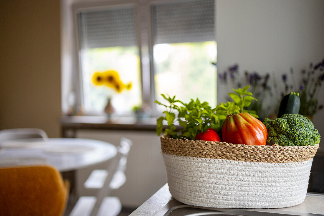 Frisches Gemüse in einem Weidenkorb auf einer Arbeitsfläche in einer hellen Küche vor einem unscharfen Hintergrund