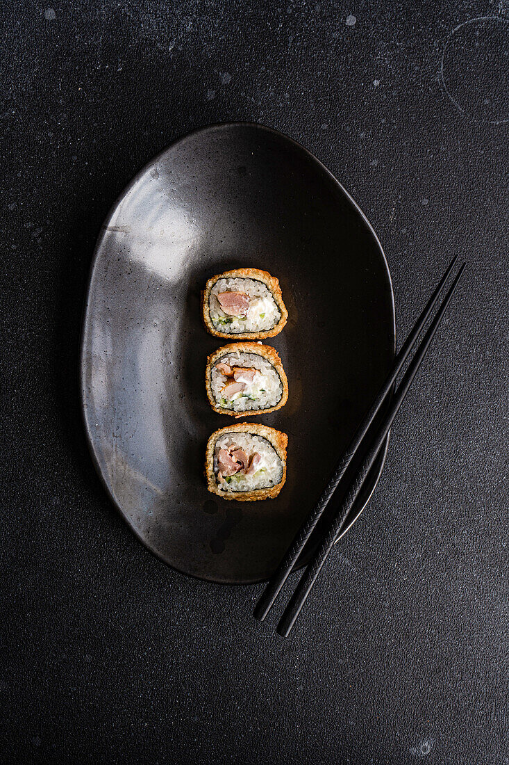 Von oben Reihe von leckeren gebratenen Sushi-Rollen mit gekochtem Reis und Lachs mit Avocado-Scheiben auf schwarzem Keramikteller auf Tisch