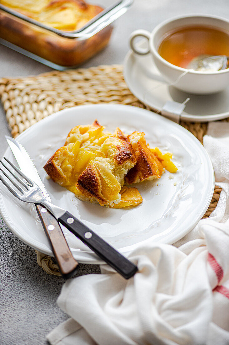 High angle of seasonal piece of peach pie served on plate with fork and knife and cup of tea placed on table near napkin against blurred background