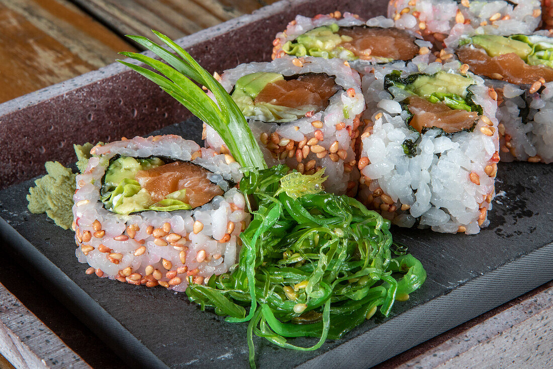 Closeup of served set of avocado tuna uramaki sushi rolls with wakame salad on side on concrete plate