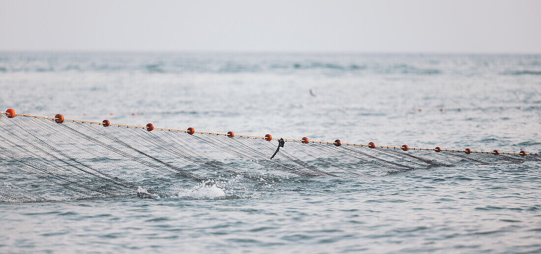 Scenic view of waving rippling seawater splashing fishing net with rope tied with red cork floats on sunny day of summer against blurred cloudless sky