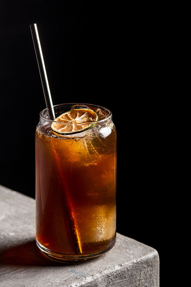 Erfrischender alkoholischer Cocktail im Glas mit Eiswürfeln und Strohhalm, garniert mit einer getrockneten Limettenscheibe, auf einem Steintisch
