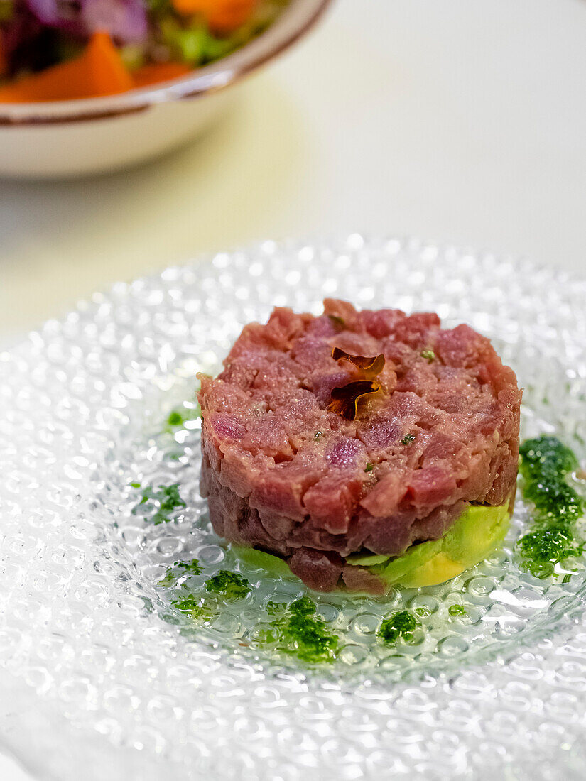 High angle of delicious Mediterranean tuna tartare with avocado and placed on glass plate with green leaves and served on table near crop fruit salad in daylight