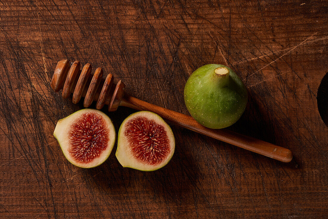 A top-down view of ripe figs beside a honey dipper on an old, textured wooden surface, evoking rustic culinary charm.