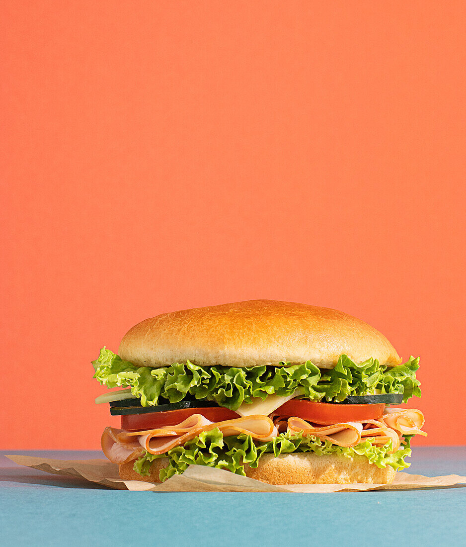 Delicious sandwich with ham, tomatoes, cucumber and cheese slices and fresh lettuce on blue and orange background