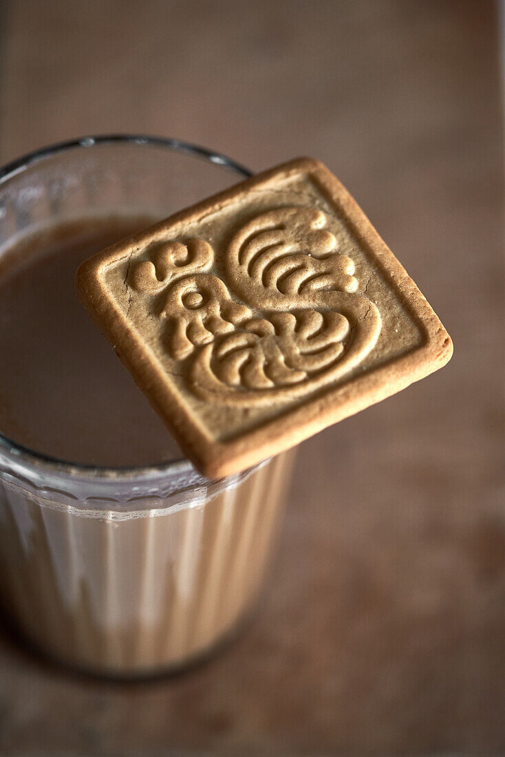 Close-up of a square cookie with detailed embossing perched on a full glass of chocolate milk