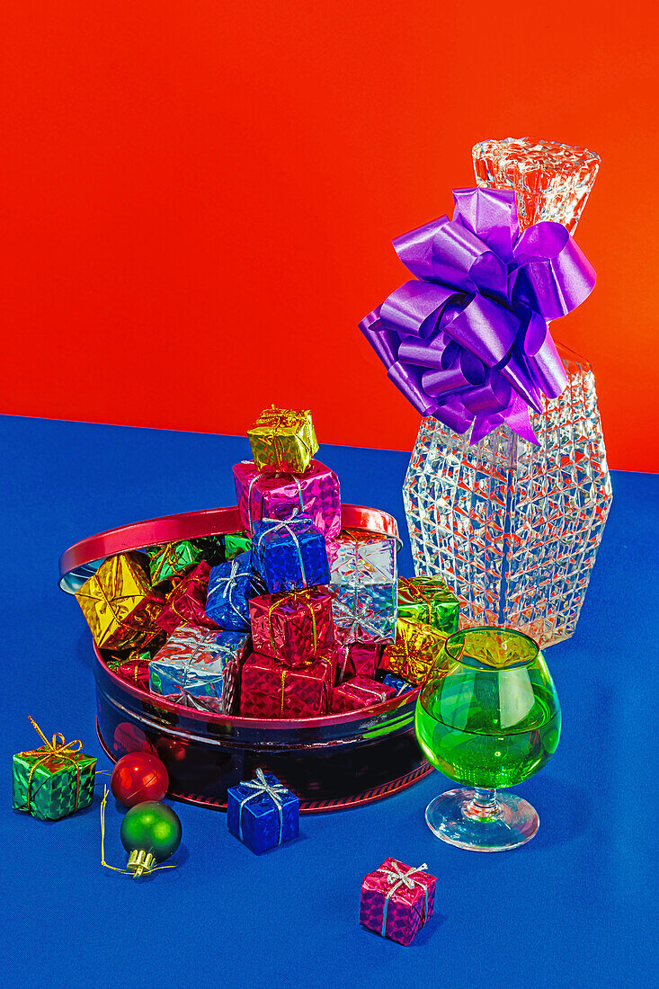 Bunte Weihnachtsgeschenke, die aus einer Schale auf einem blauen Tisch überlaufen, mit einem großen Geschenk im Hintergrund vor einem roten und blauen Hintergrund