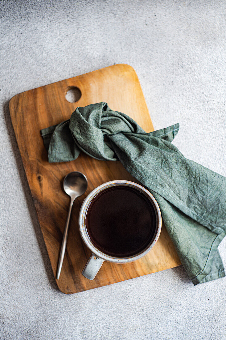 Top view of cup of coffee placed on wooden tray with napkin and spoon against gray surface