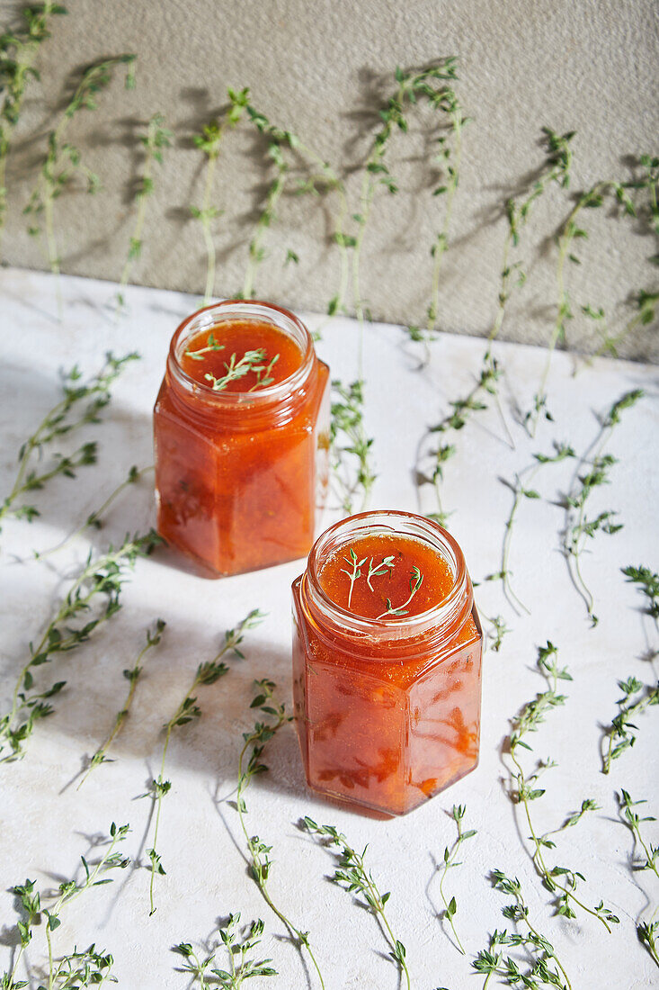 Mit hausgemachter Fruchtmarmelade gefüllte Gläser stehen auf einem Tisch mit grünen Thymianzweigen