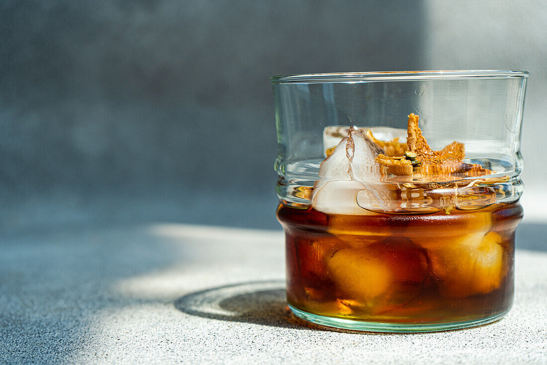 Closeup of glass of whiskey with ice and orange peel placed on gray background