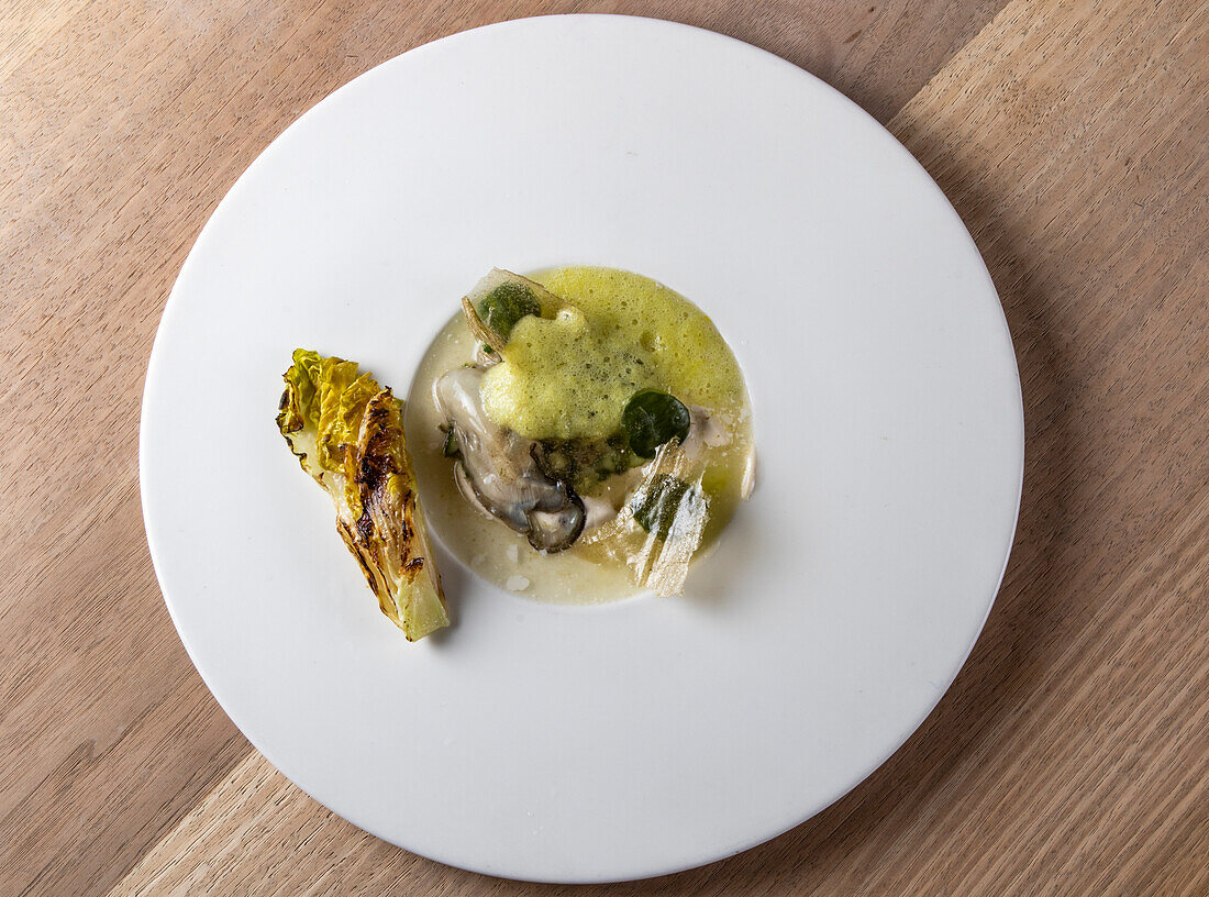 Draufsicht auf appetitliche Meeresfrüchte mit Aubergine und gegrilltem Salat, serviert auf einem weißen Teller auf einem Holztisch