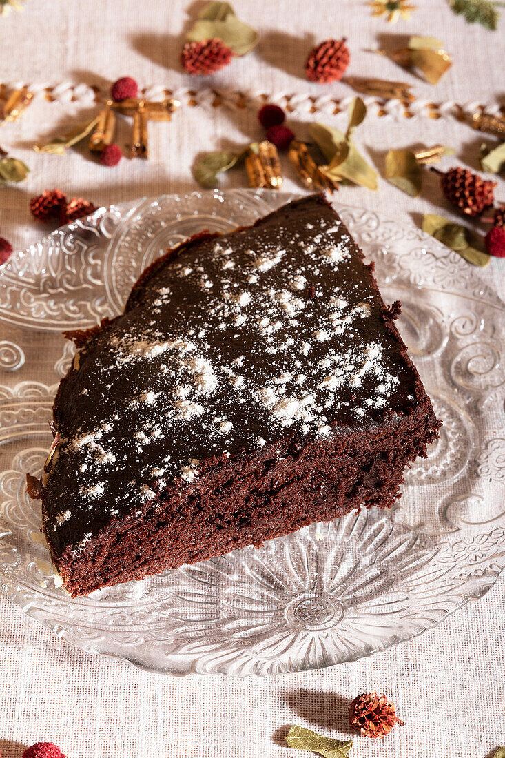 High angle of A slice of moist chocolate cake dusted with powdered sugar, presented on an ornate glass plate with a floral backdrop