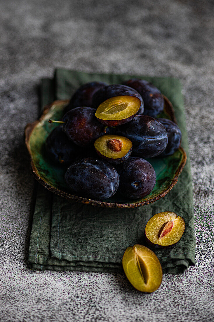 High angle of organic ripe plums served in marble bowl placed on napkin on gray surface